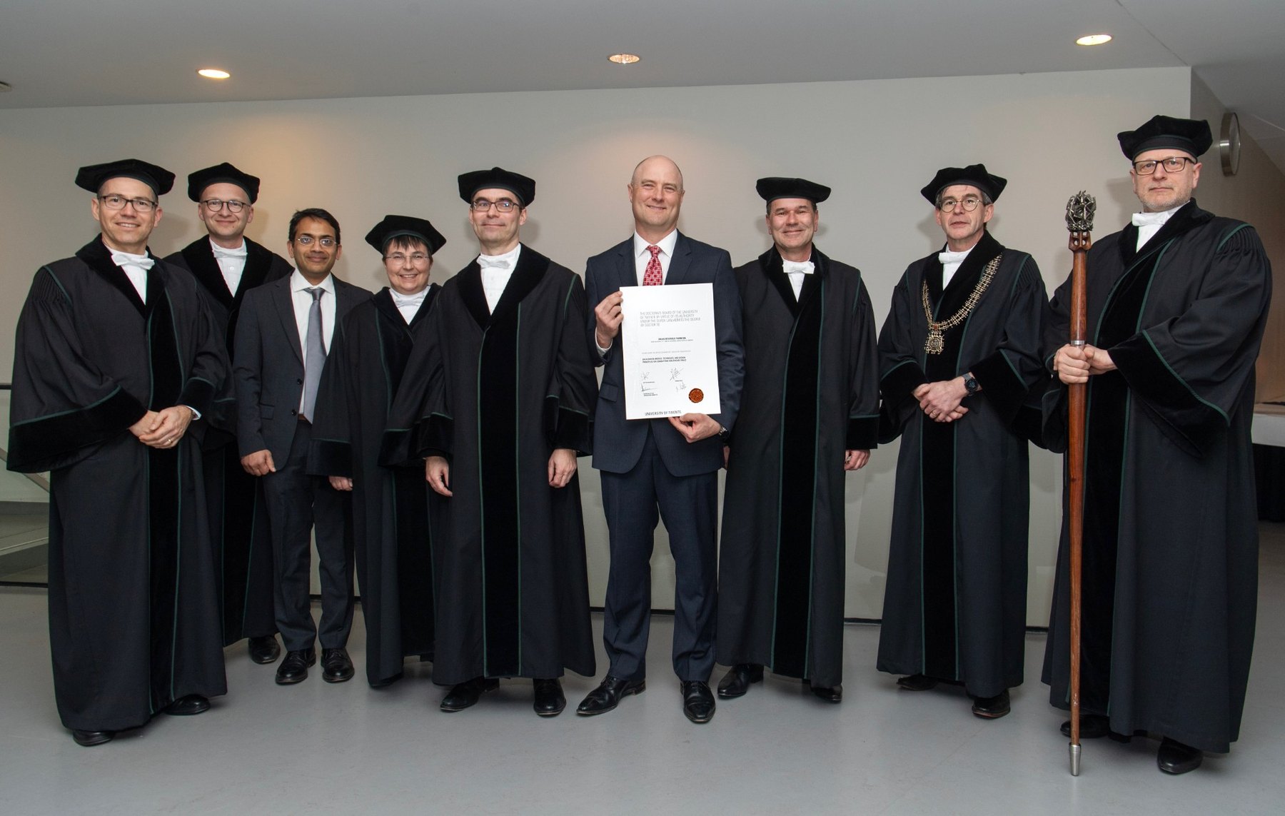 Dallas Thornton holding his doctoral certificate, surrounded by the doctoral committee in academic gowns