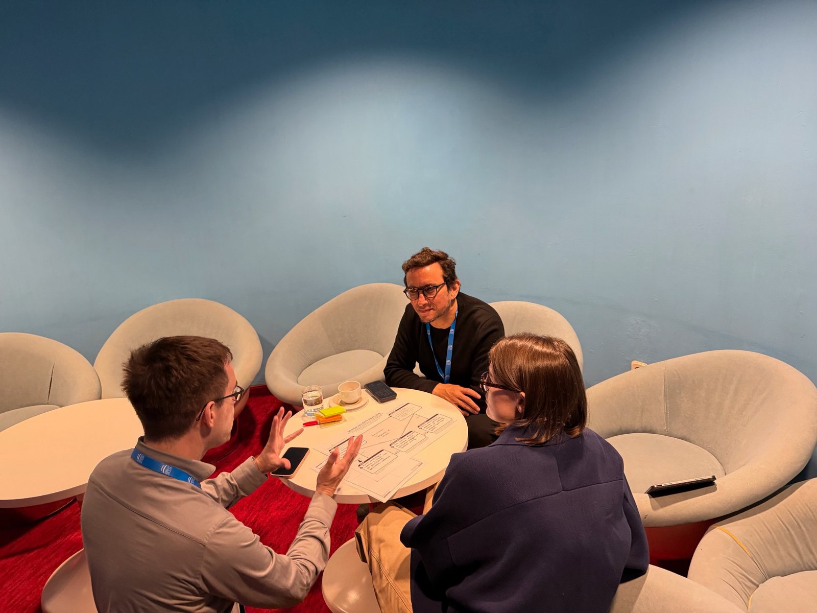 Three workshop participants around a small round table discussing a filled-in Design Validity Envelope worksheet with sticky notes