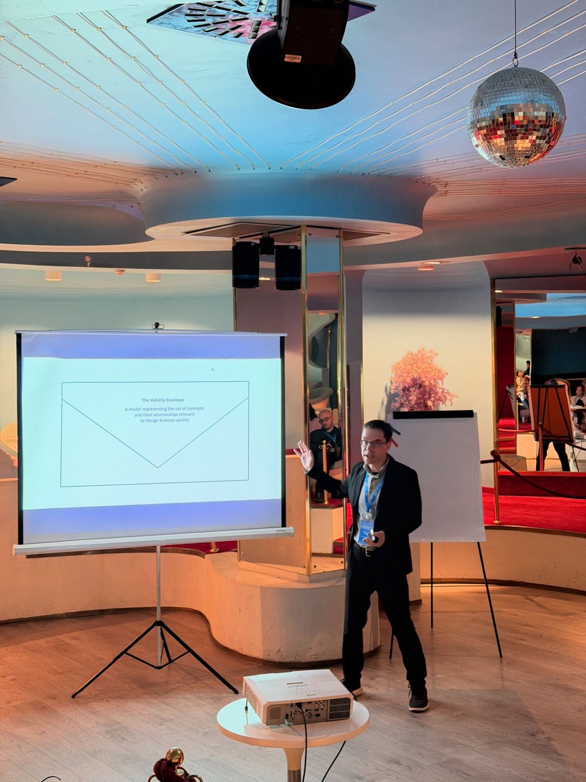 Roland M. Mueller presenting the slide The Validity Envelope, a model representing the set of concepts and their relationships relevant to design science validity, on a projection screen